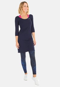 Abito navy a lunghezza ginocchio con maniche a tre quarti, sovrapposto a leggings blu a motivo. Sneakers bianche completano l'outfit.