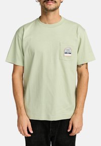 Helle grüne Baumwoll-T-Shirt mit rundem Halsausschnitt, kurzen Ärmeln und einer Brusttasche, die ein mehrfarbiges Palmenbaum-Logo zeigt.