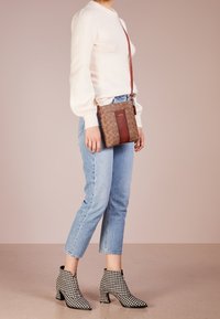 Brązowa torebka na ramię z jasnobrązowym geometrycznym wzorem, kontrastującym bordowym paskiem oraz długim regulowanym paskiem. Posiada zamek błyskawiczny.