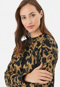 Leopard-mønstret bluse i guld og sort; lange ærmer, høj hals, glat tekstur, med et dristigt, abstrakt mønster.