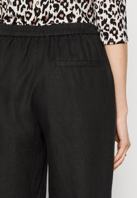 Zwarte linnen broek met elastische tailleband en een enkele achterzak. De stof heeft een subtiele textuur, geschikt voor casual kleding.