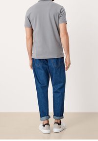Polo gris avec un col, associé à un pantalon en denim bleu. La tenue présente des poignets retroussés et des baskets blanches avec des accents noirs.
