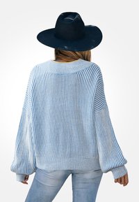 Jasnoniebieski sweter w paski o prążkowanej powierzchni, w luźnym kroju i z szerokimi rękawami. Połączony z jasnoniebieskimi dżinsami i czarną czapką.