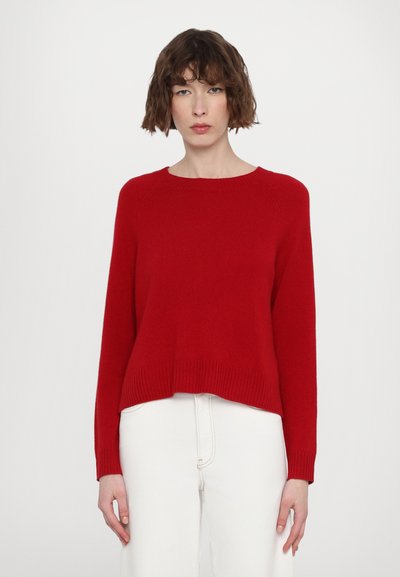 Pull en maille rouge avec un col rond, des épaules tombantes et un ourlet côtelé. Associé à un jean écru. Coupe confortable et texture légère.
