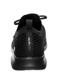 Musta verkkomallinen urheilukenkä, jossa on teksturoitu neulekuvio, pyöreä korko ja vetonauha takana. Varustettu pehmeällä pohjalla ja vähäisellä brändäyksellä.