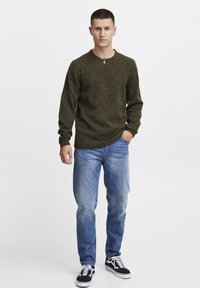 Dunkelgrüner Strickpullover, langärmlig, Rundhalsausschnitt. Hellblaue Jeans, leicht tailliert. Schwarz-weiße karierte Sneaker. Einfaches Design.