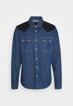Langærmet mørkeblå denimskjorte med sort skulderstykke, trykknapper foran og to brystlommer med trykknapklapper.