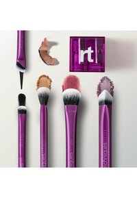 Cinq pinceaux de maquillage violets avec des têtes de pinceau différentes, des poudres de maquillage étalées, et un taille-crayon double violet étiqueté "rt".