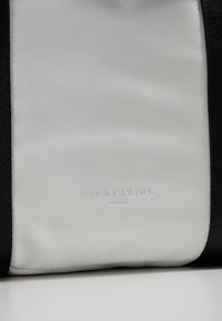 Panneau en cuir blanc doux avec une texture subtile et le logo "LIEBESKIND BERLIN" embossé, bordé de bords en tissu noir.