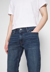 Jeans de denim en azul oscuro, con un corte recto y un diseño clásico de cinco bolsillos, con costuras en contraste y cierre de botón metálico.