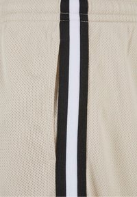 Tissu en maille beige avec des bordures verticales rayées noires et blanches, montrant une ouverture de poche latérale sur les vêtements.