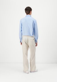 Camisa de botones azul claro de mangas largas combinada con pantalones sueltos de color crema y zapatillas blancas con acentos rojos.