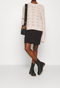 Suéter de punto rosa claro con un patrón de ondas, combinado con una falda vaquera negra con una abertura frontal y botas de combate negras con cordones.