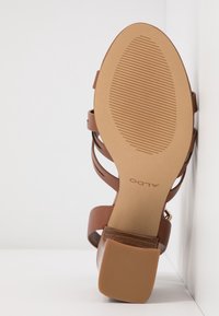 Sandale marron à talon avec une semelle beige texturée. Caractérisée par des lanières fines et un talon carré, présentant une finition en cuir lisse.