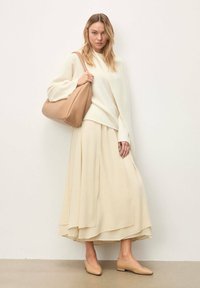 Pull cache-cœur couleur crème, jupe fluide crème et ballerines beige clair. Le mannequin porte un sac à main marron clair, doux et texturé.