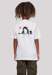 White cotton t-shirt featuring a black graphic of an arch and a red sun, with "ESCAPE" text below. Back view shows relaxed fit, short sleeves.