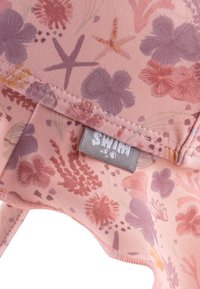 Patterned swim cap featuring soft pink fabric with floral designs in purple and orange, plus a gray logo tag stitched on the interior.