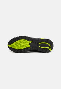 Black athletic shoe sole with a yellow-green rubber traction pattern, featuring deep grooves and a curved heel design for stability.