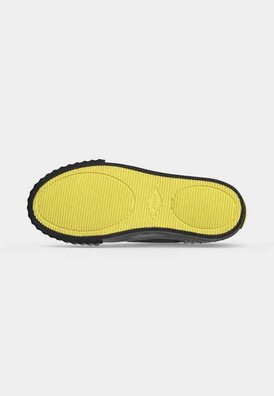 Semelle de chaussure avec zone de grip texturée jaune et bord extérieur noir, montrant le logo de la marque "Adtex" au centre.
