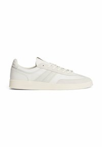 Zapatillas blancas que combinan cuero y tela, con cordones en tonos similares, tres franjas sutiles en el lado y una suela de goma texturizada.