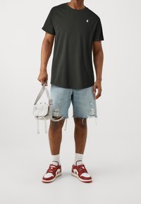 Musta lyhythihainen T-paita, vaaleansiniset revenneet farkkushortsit, punaiset ja valkoiset lenkkikengät, harmaa olkalaukku säädettävällä hihnalla.