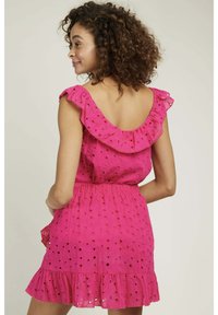 Robe sans manches rose avec un col froncé, dotée de motifs œillets et d'une taille cintrée. La jupe a un ourlet évasé.