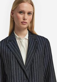 Marinblå kavaj med smal randig design, kantsydd krage och enspännings-knäppning, parat med en vit skjorta med krage.