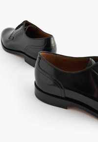 Chaussures habillées en cuir noir avec une finition brillante, présentant un design à lacets, une texture lisse, et un talon bas avec des détails de couture subtils.