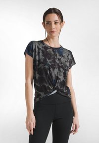 Dunkel mit Blumenmuster bedrucktes T-Shirt aus weichem Stoff, mit vorne geknotetem Detail und lockerem Schnitt, kombiniert mit schwarzen Leggings.