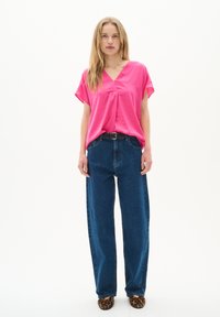Top rosa a maniche corte con scollo a V, abbinato a jeans a vita alta blu a gamba larga e ballerine maculate. Design pulito e minimal.