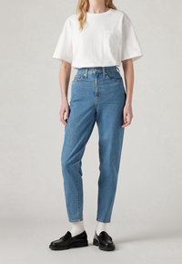 Vaqueros de talle alto en azul claro con un ajuste relajado, combinados con una camiseta blanca de cuello redondo y mocasines negros, presentan bolsillos estándar.
