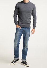 Maglione grigio a maniche lunghe con polsini e orlo a costine, abbinato a jeans blu leggermente strappati e sneaker nere con suola bianca.