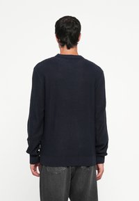 Pull en maille bleu marine avec un motif texturé, manches longues et ourlet côtelé. Le dos présente un design classique avec encolure ronde.
