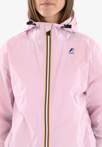 Veste imperméable rose clair avec un devant zippé arborant un motif rayé audacieux en noir, jaune et blanc ; comprend une capuche ajustable.