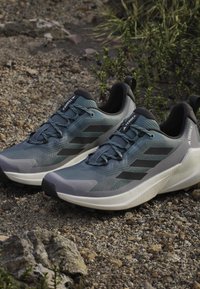 Blaue und graue Sportschuhe mit einem Obermaterial aus Mesh, schwarzen Akzenten, strukturiertem Sohlen und reflektierenden Elementen. Designed für Outdoor-Aktivitäten.