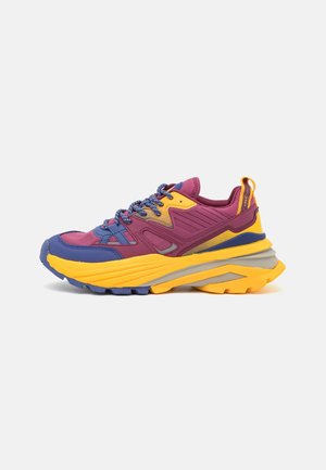 Colorful sneaker featuring a purple, yellow, and blue upper, textured fabric, thick multi-layered sole, and contrasting laces.