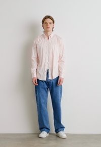 Cămașă roz deschis, cu nasturi, croi lejer, purtată împreună cu blugi denim albaștri, largi, și tenisi albi. Design simplu, textură netedă și stil casual.
