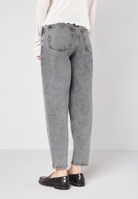 Graue Denim-Hosen mit hohem Bund und lässiger Passform, die eine verblichene Textur, fünf Taschen und Kontrastnähte aufweisen. Umschlagabschlüsse an den Knöcheln.