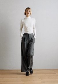 White long-sleeve turtleneck top paired with high-waisted, wide-leg gray trousers. Black shoes complete the outfit, set against a neutral background.