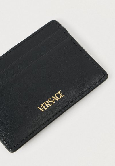 Μαύρο πορτοφόλι από δέρμα με τέσσερις θήκες καρτών και ανάγλυφο χρυσό λογότυπο "VERSACE" στο μπροστινό μέρος. Ομαλή υφή, μίνιμαλ σχεδίαση.