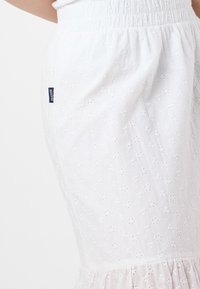 Gonna bianca realizzata in tessuto leggero con motivo floreale ricamato a occhiello. Presenta una vita elasticizzata arricciata e un orlo a balze.