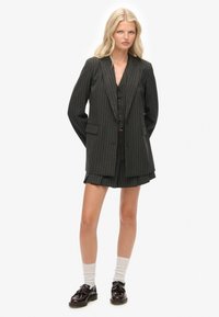 Mørkegrå pincetternet blazer med skræddersyet pasform, dobbeltradet design og to forlommer. Matchende med en kort nederdel.