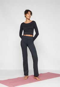 Black cropped long-sleeve top and dark gray yoga pants, featuring a smooth texture. The model stands barefoot on a pink yoga mat.