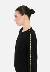 Zwarte sweatshirt met een ronde halslijn en een verticale lijn van decoratieve versieringen langs de rechtermouw.