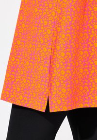 Rosa klänning med orange leopardmönster, med en framspalt och en slät textur, bärs över svarta leggings.
