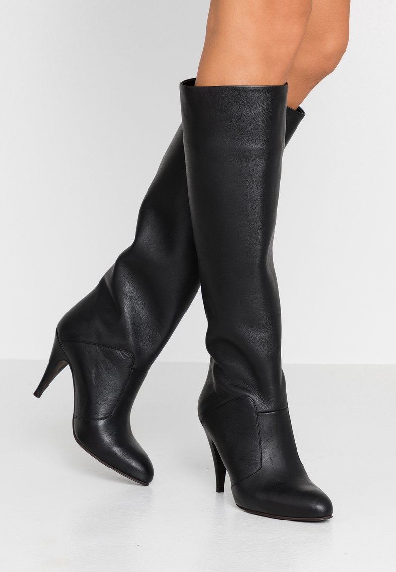Černé kožené vysoké boty po kolena s přiléhavým tvarem, špičatou špičkou a 10 cm vysokým jehlovým podpatkem. Hladká textura, minimální kování, elegantní design.