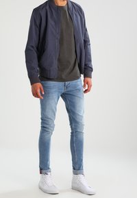 Marinfärgad bomberjacka, grå t-shirt, ljusblå skinny jeans och vita sneakers. Jackan har en framzip och ribbade muddar.