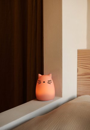Lampa i form av en katt i mjukt rosa silikon med matt finish, med svarta morrhår och ett subtilt sken, placerad på en ljust färgad hylla.