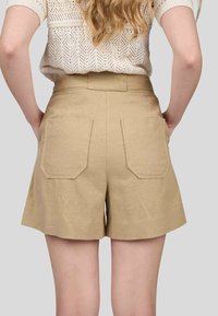Shorts en kaki avec une texture lisse, taille haute et deux grandes poches arrière. Le design présente une apparence épurée et ajustée.