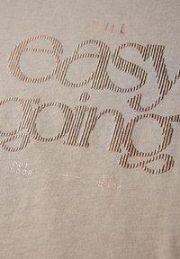 Tejido beige con texto en relieve en un diseño a rayas; las frases incluyen "EL que se toma la vida con calma" y "EXTERIOR" en un metálico color oro rosa.